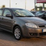 Szary Fiat Bravo zaparkowany przed salonem samochodowym na brukowanym placu